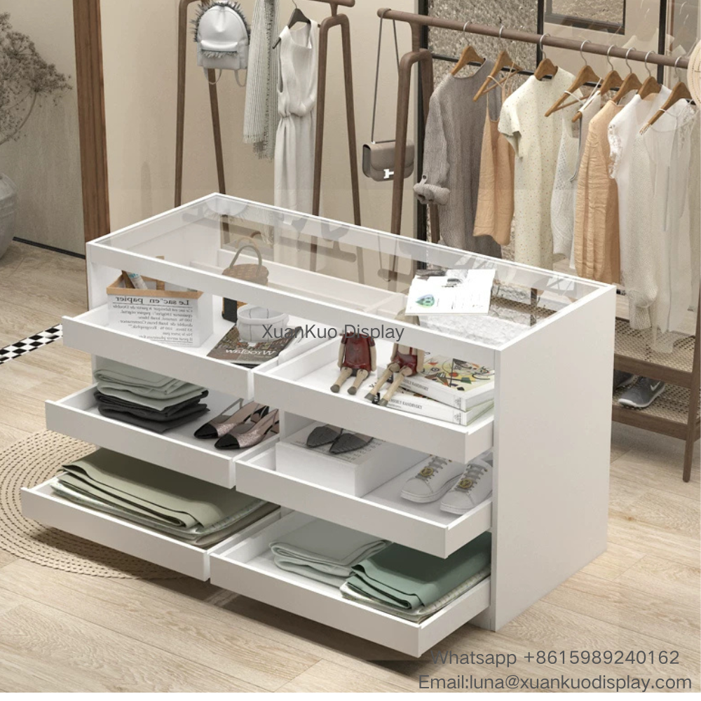 minimalist white clothing store display cabinet, transparent glass top, multiple pull-out divided drawers, multi-compartment storage for folded clothes, shoes and accessories, central display island for women fashion apparel boutique