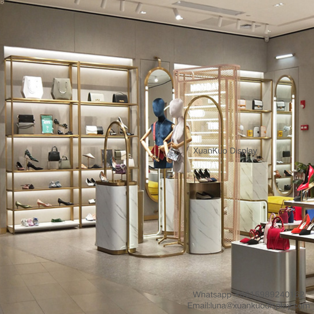 luxury shoe and handbag store display furniture set, gold metal frame backlit wall display shelves for footwear and leather bags, marble pattern cylindrical display plinths, arched gold mirror mannequin stands, perforated metal partition for women fashion leather goods boutique
