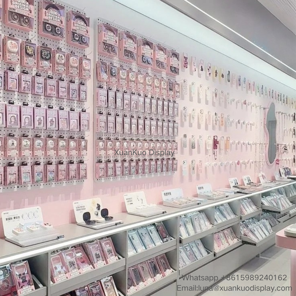 pastel pink phone accessory store display furniture set, large perforated pegboard wall panel for earphones, charms and packaged phone cases, white tiered display counter with pull-out drawers, built-in top LED light strip for mobile gadget boutique
